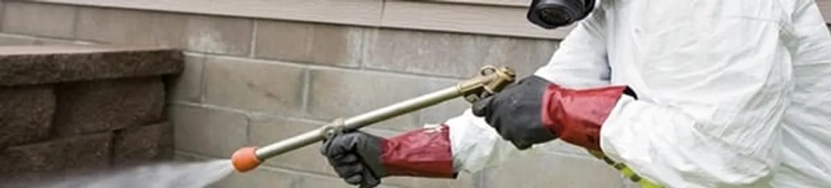 Pest control technician applying exterior insect treatment along a home foundation in Knoxville, TN
