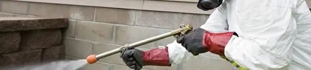 Pest control technician applying exterior insect treatment along a home foundation in Knoxville, TN
