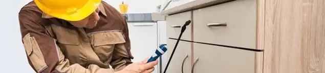 Roach exterminator applying treatment under kitchen cabinets in Knoxville, TN