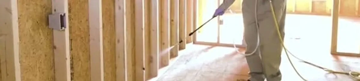 Termite treatment technician applying spray along framing and unfinished walls in Knoxville, TN